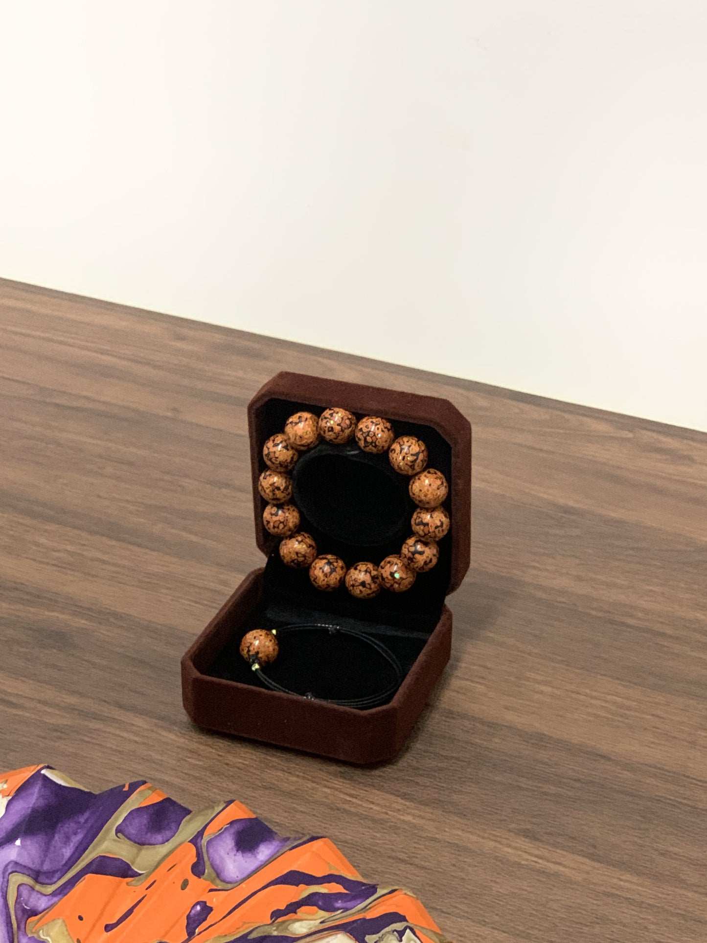 LanHeal Couple Bracelets in a storage box, placed beside a part of an opening folding fan on wooden table.